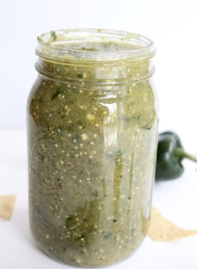 Clear jar holding green salsa. Pictures of jalapeños behind jar.