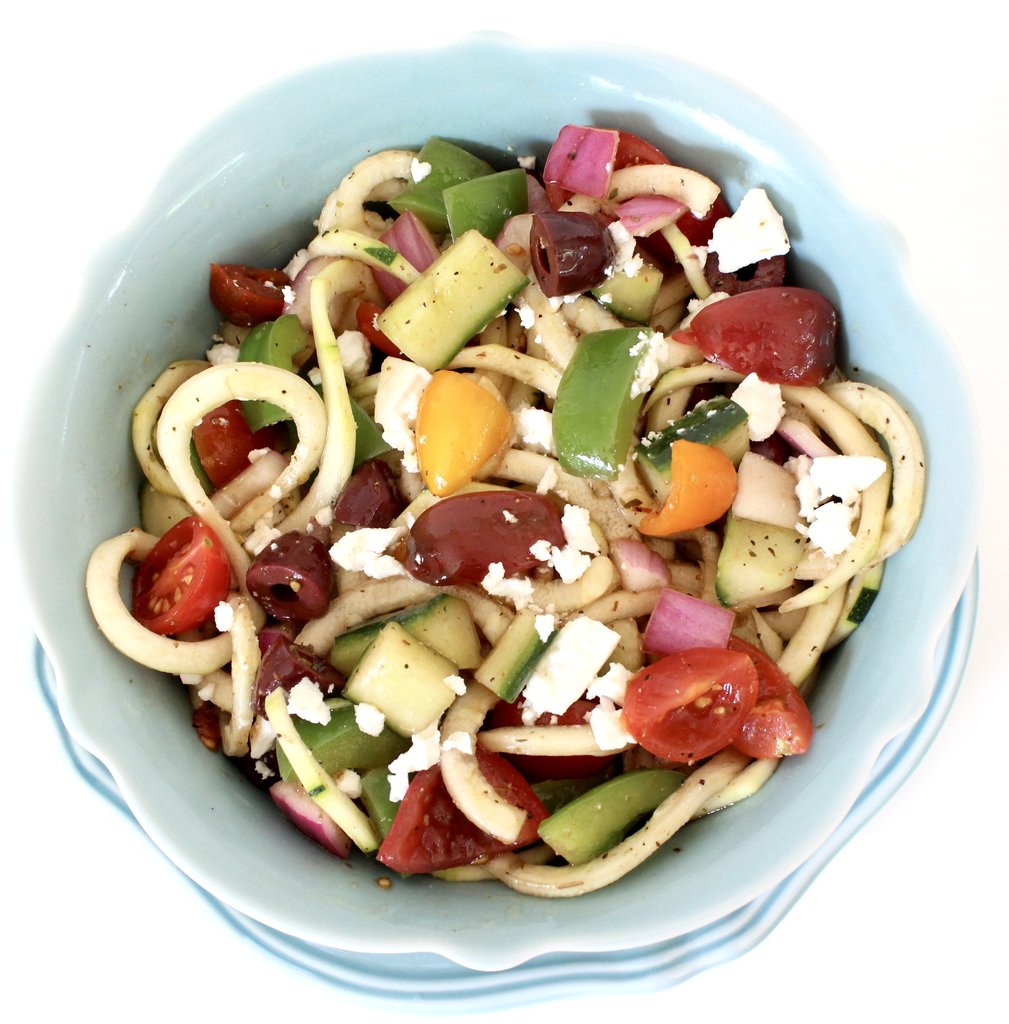Blue bowl filled with zucchini noodles, green peppers, tomatoes, cucumbers, and onions.